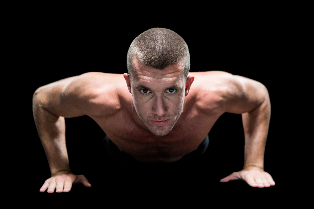 Portrait of confident shirtless athlete doing push ups against black background